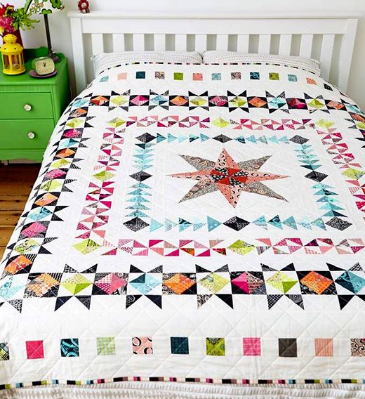 a bed with a quilt on top of it next to a green dresser and white headboard