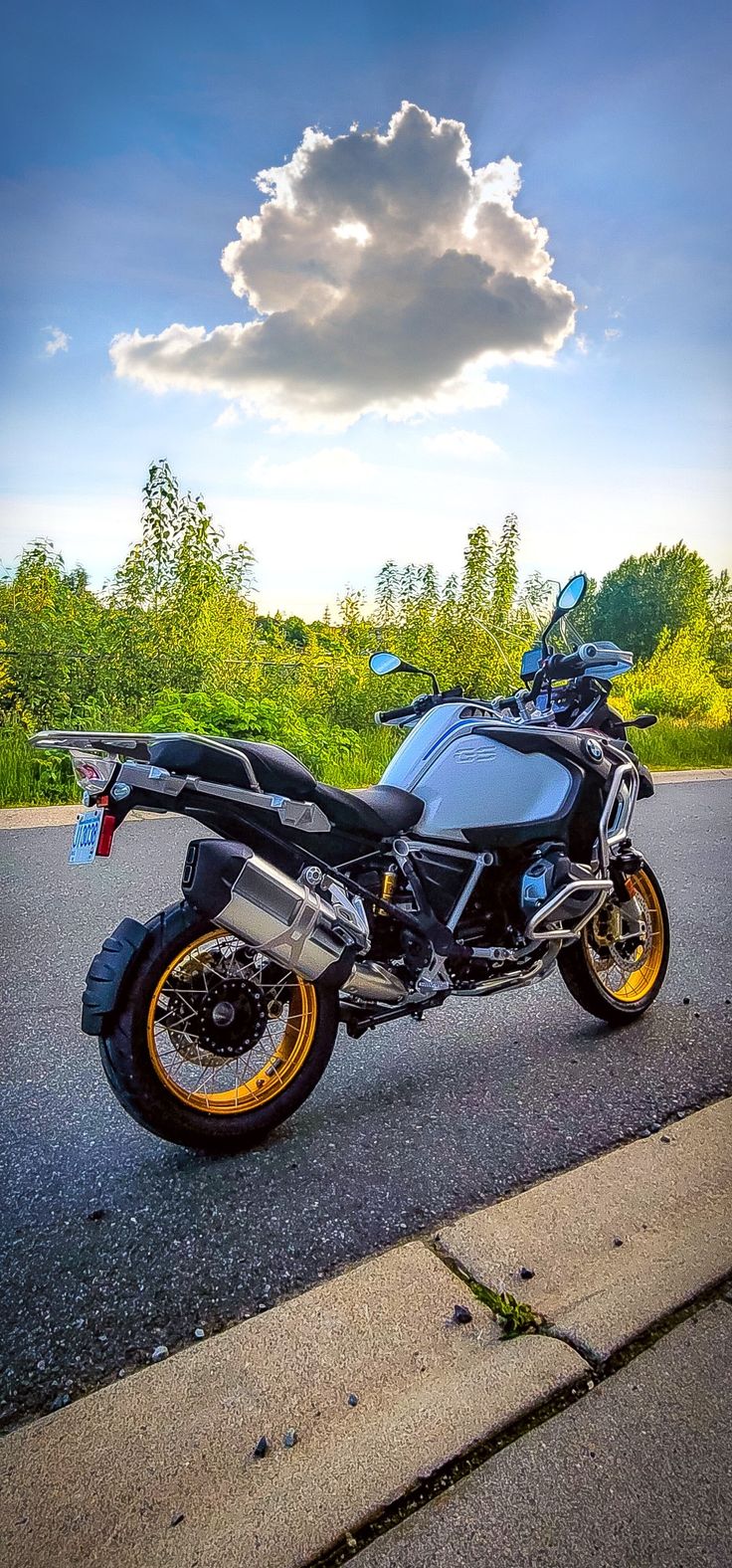 the motorcycle is parked on the side of the road in front of some grass and trees