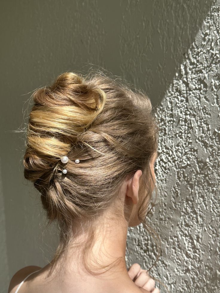 Model with blonde hair shows off modern textured french twist roll style up-do for a Bridal photoshoot. Upstyle features pearl pins in various sizes Middle Part French Twist, Updo With Pearl Pins, French Twist With Pearls, French Twist Wedding Hair With Veil, Bridal Updo Pearls, Bridal French Twist With Veil, Pearl Updo, French Twist With Veil, Bridal French Twist