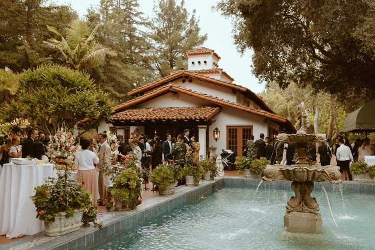 a group of people standing around a pool next to a building with a fountain in front of it