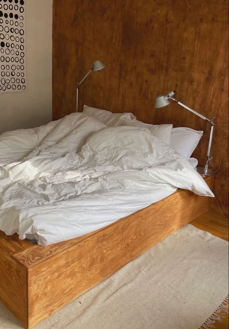 an unmade bed with white sheets and pillows on it in front of a wooden headboard