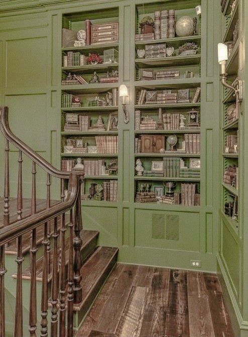 a green bookcase with lots of books on it and stairs leading up to the second floor