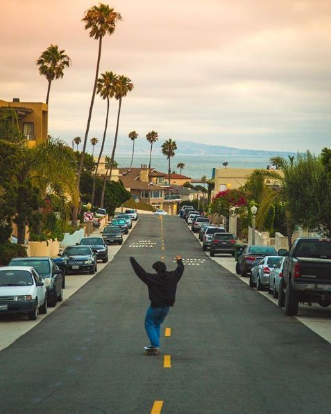 a person riding a skateboard down the middle of a street next to parked cars