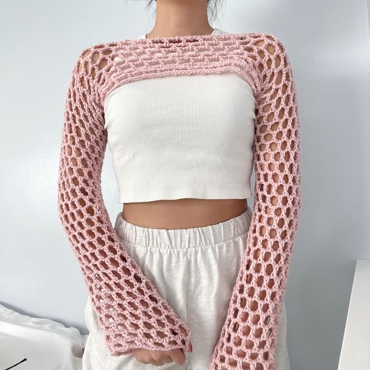 a woman standing in front of a white wall wearing a pink knitted sweater and matching pants