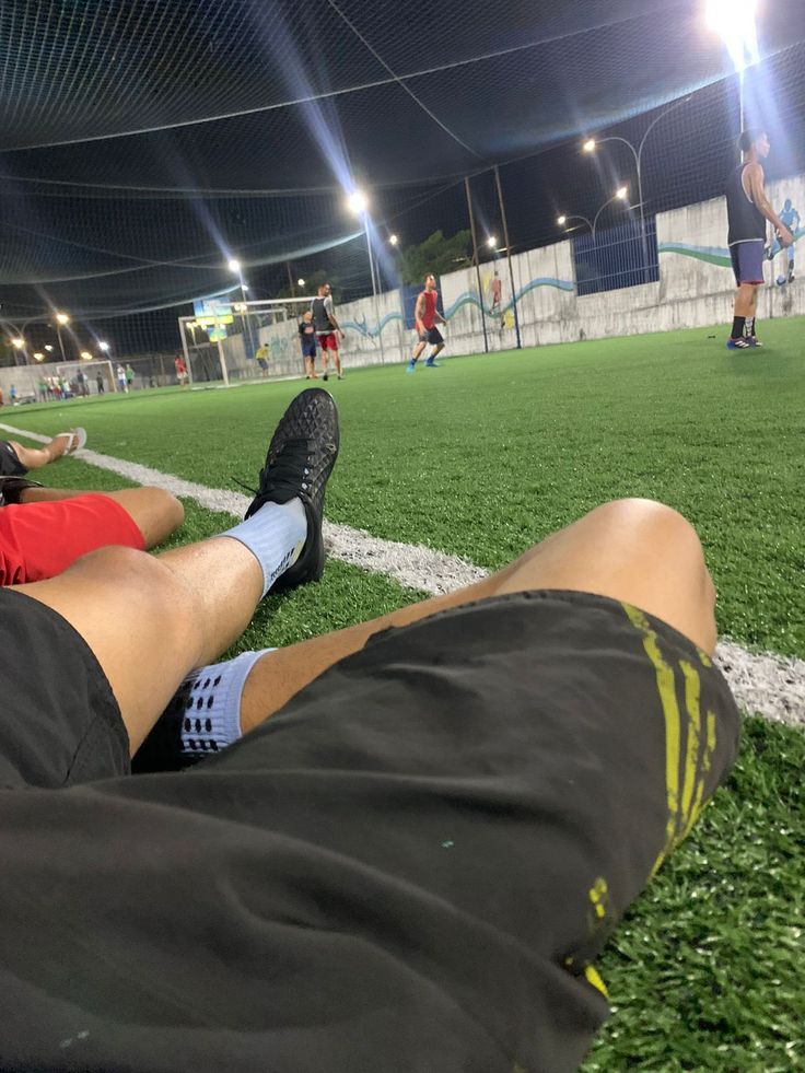 two people are sitting on the grass at night playing soccer with their feet up in the air