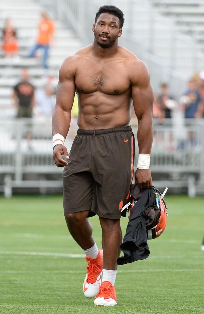 a shirtless man walking on the field at an orange and white football game with his hand in his pocket