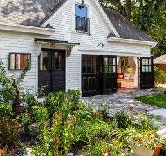 a white house with black doors and windows in the front yard, surrounded by greenery