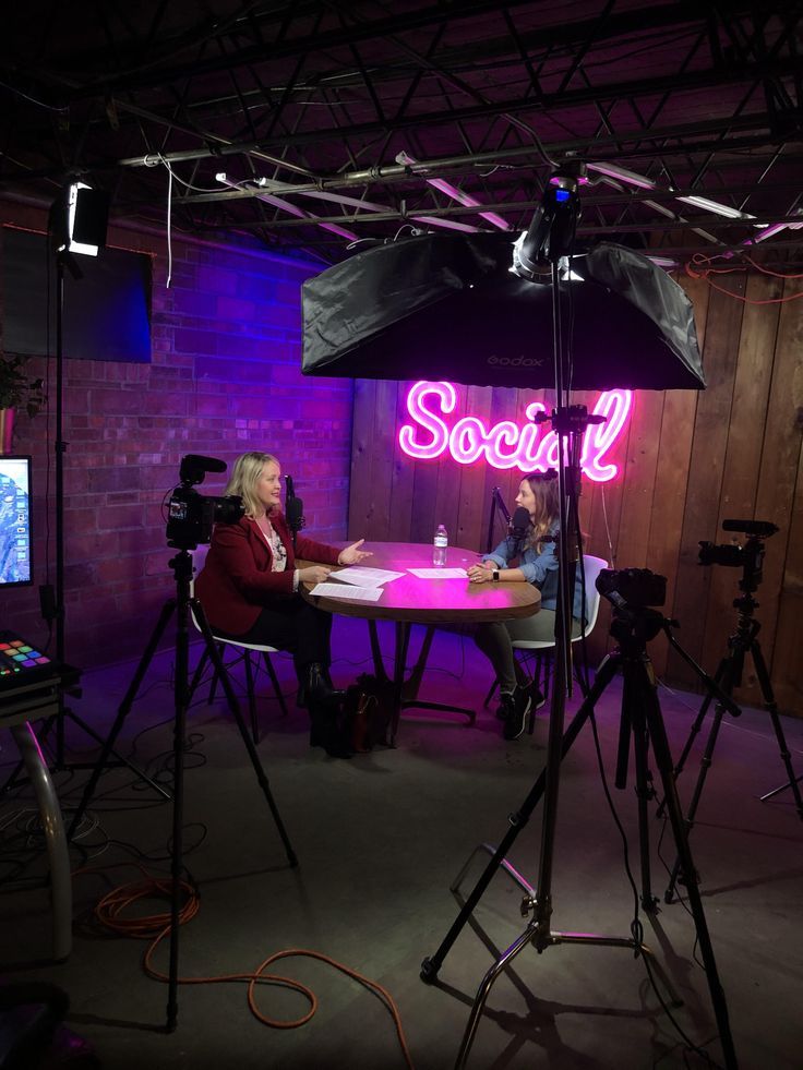 two people sitting at a table in front of a camera set up for a video