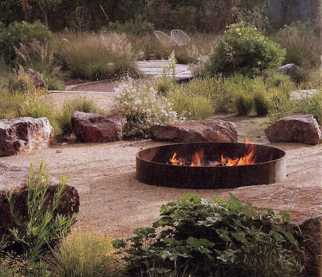 an outdoor fire pit surrounded by rocks and plants