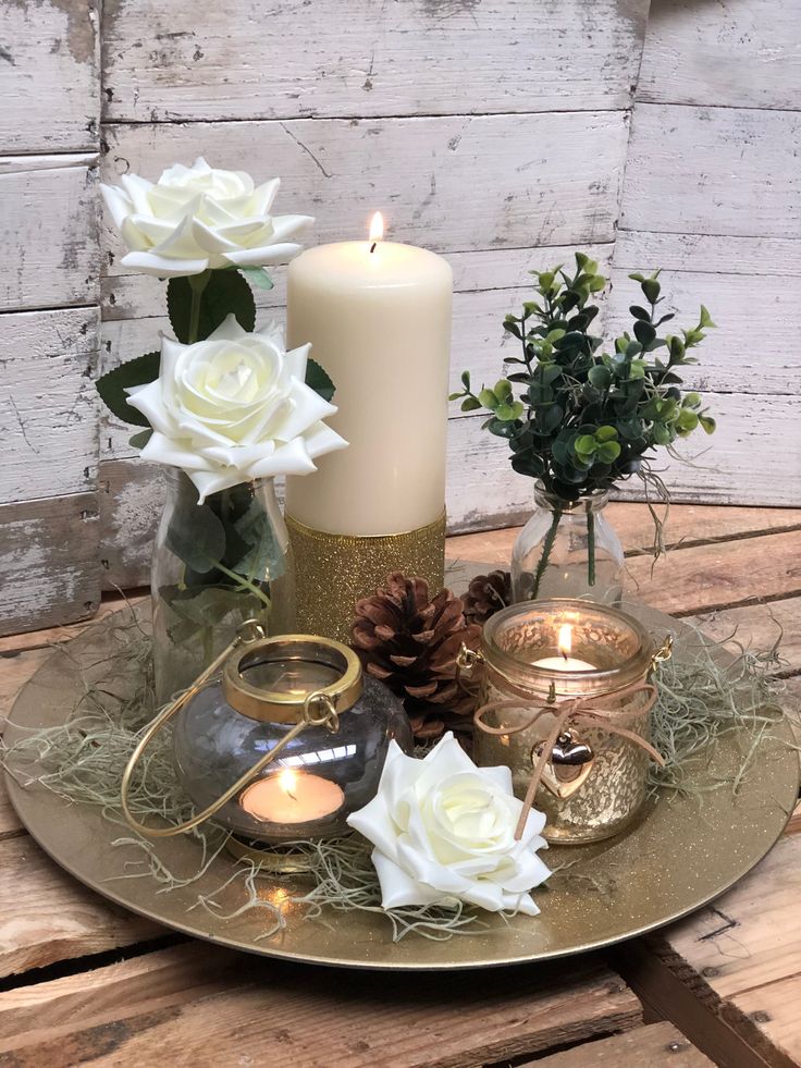 a candle and some white flowers on a tray with pineconi, roses and candles