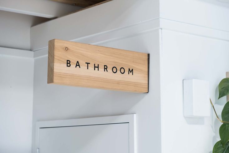 a bathroom sign mounted to the side of a white wall next to a potted plant