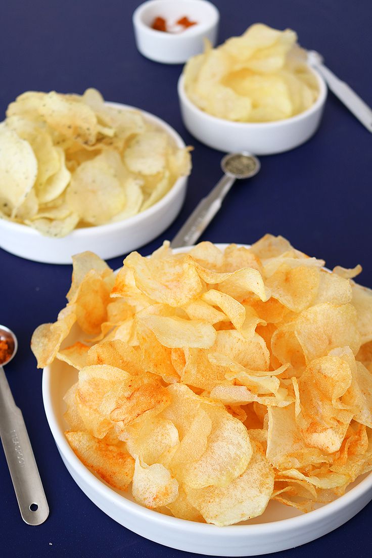 two bowls filled with potato chips next to spoons and utensils on a blue table