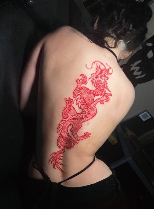 a woman's back with a red dragon tattoo on her left shoulder and right arm