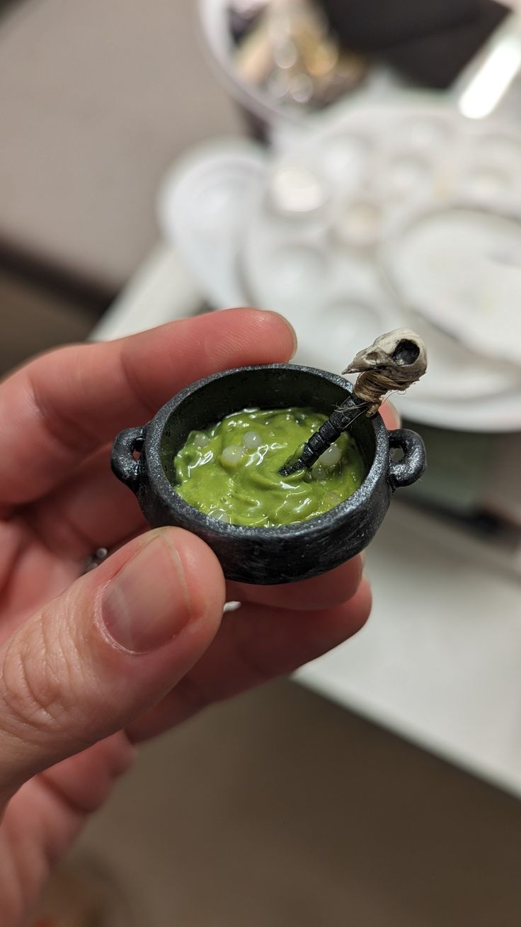 a hand holding a small black cup with green liquid in it