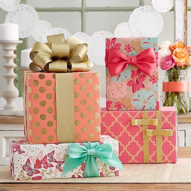 three colorful boxes with bows on them sitting on a table next to flowers and candles