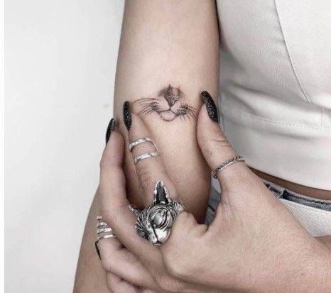 two hands holding each other with tattoos on their fingers and one has a cat's head