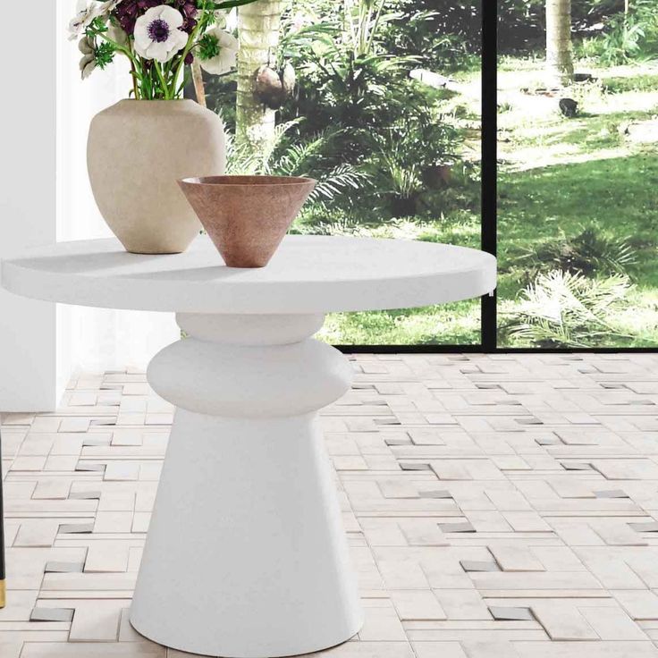 two vases with flowers sit on a white table in front of a large window