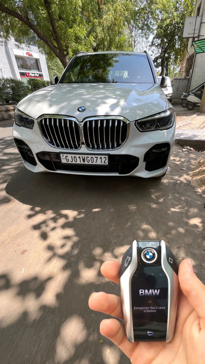 a hand holding a cell phone in front of a car on a street with trees