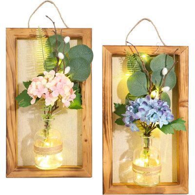 two wooden frames with flowers in them hanging from string and light bulbs on the wall