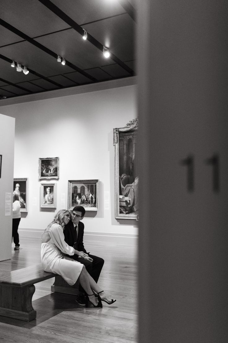 two people sitting on a bench in an art gallery