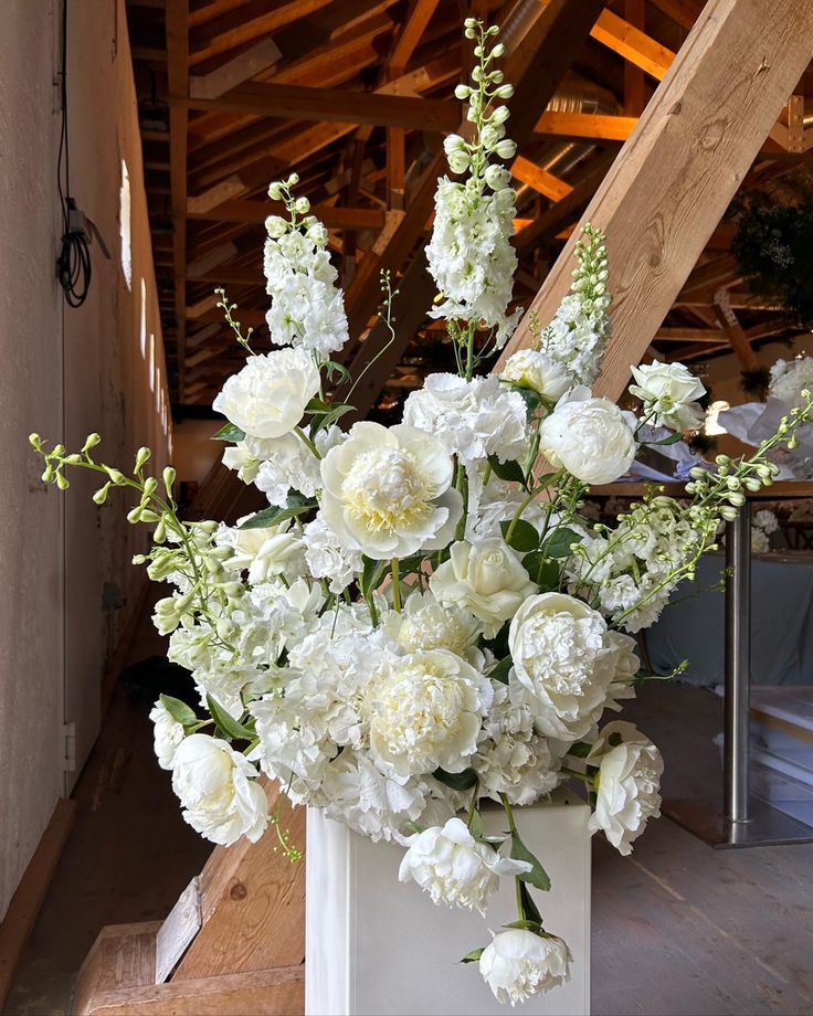 a white vase filled with lots of flowers on top of a wooden floor next to stairs