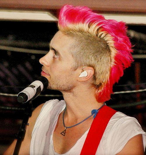 a young man with pink hair is singing into a microphone