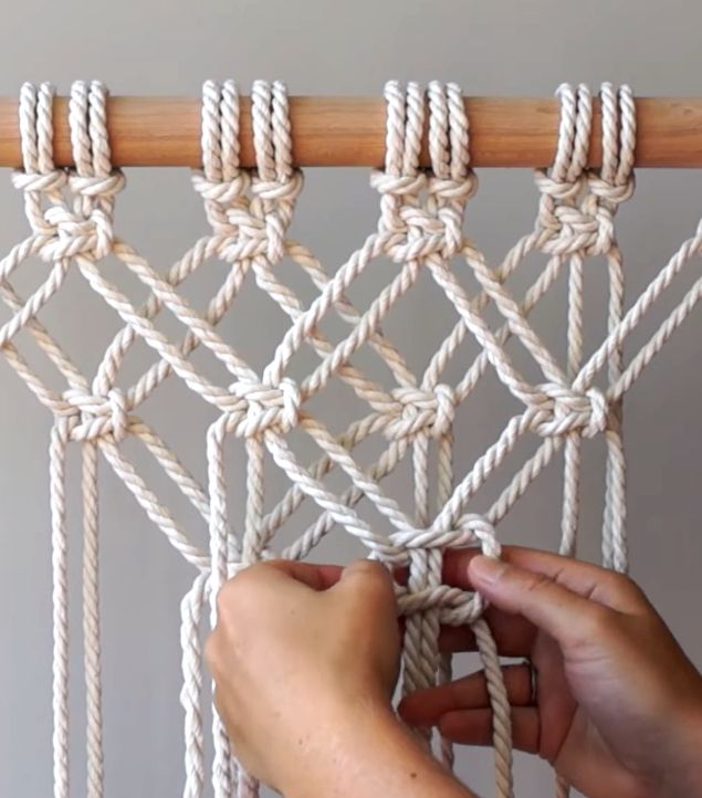 two hands are working on a macrame with ropes attached to the top of it