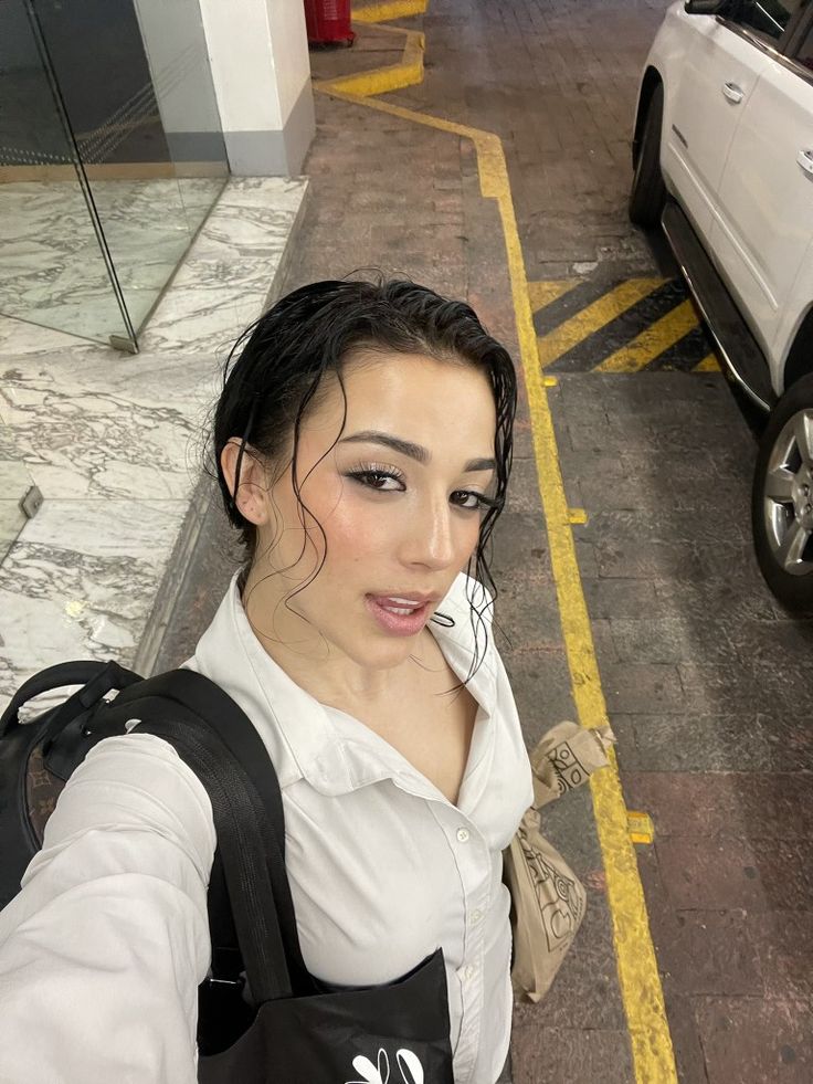 a woman taking a selfie in front of a white car on the side walk