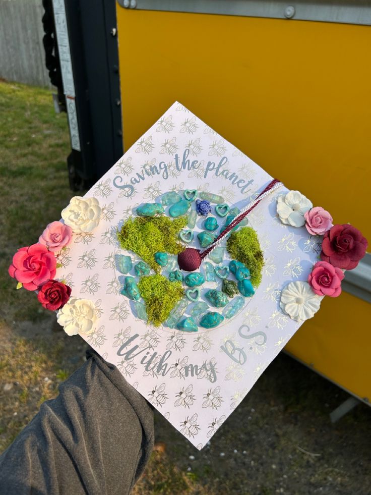 someone is holding up a graduation cap decorated with flowers and the words, saving the planet