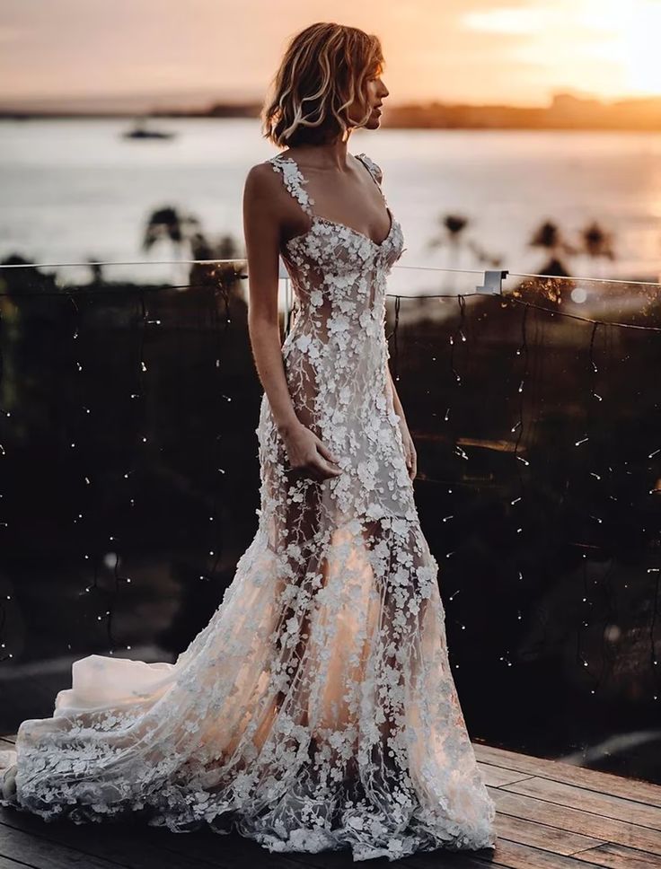 a woman in a white dress standing on a wooden deck next to the ocean at sunset