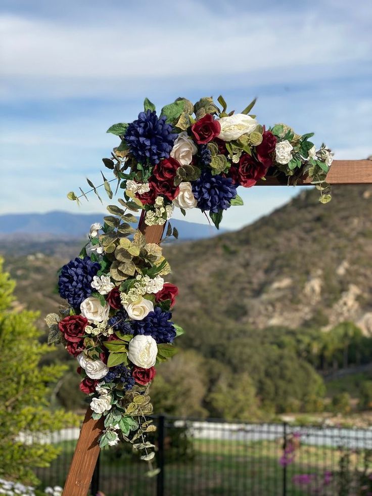 a cross decorated with flowers and greenery in the shape of a heart on top of a wooden post