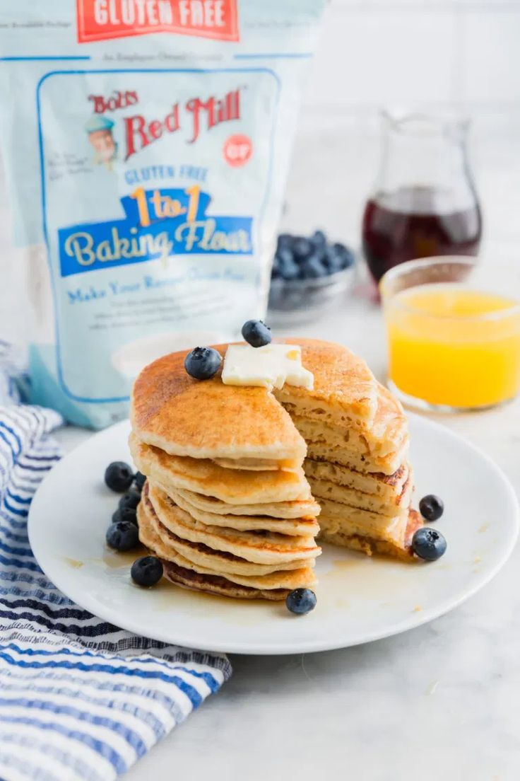 stack of pancakes with blueberries and butter on a white plate next to a bag of red mill flour