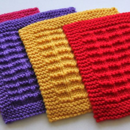 four knitted dishcloths are lined up on a table top, one is red and the other is yellow