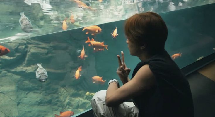 a woman sitting in front of a fish tank pointing at something with her finger to the side