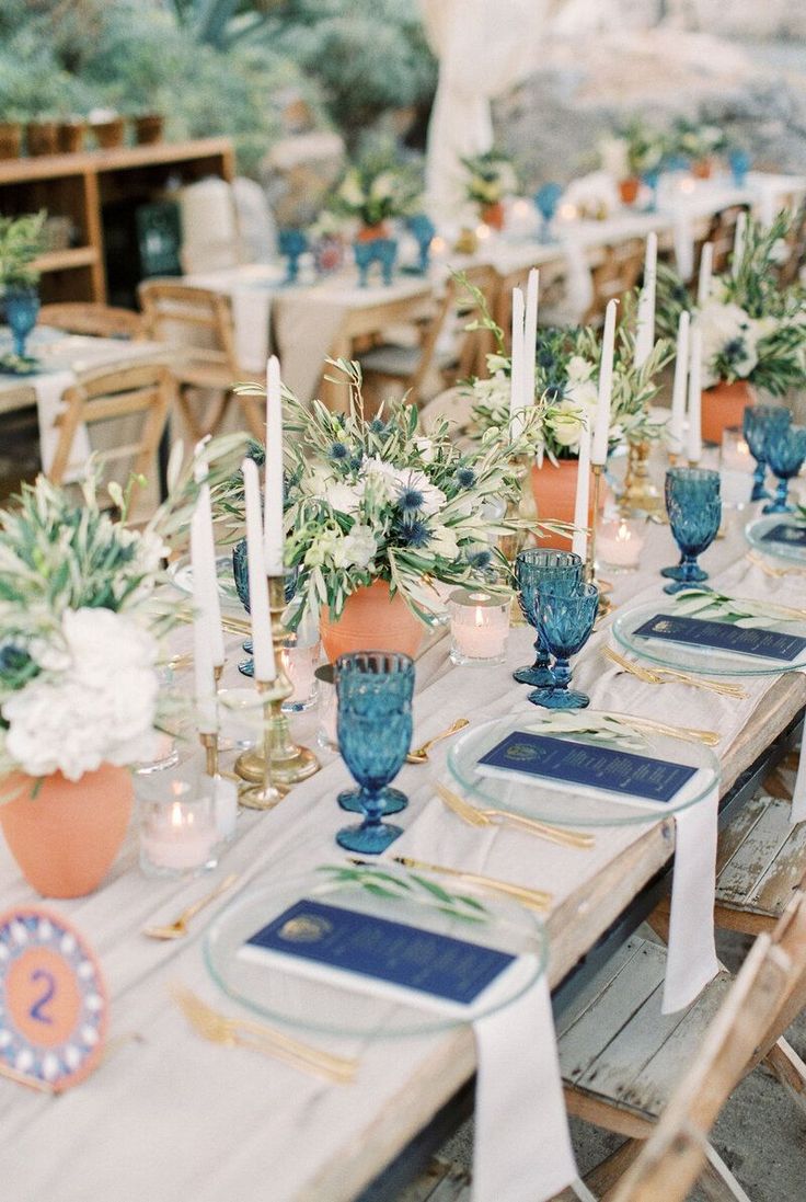 a long table with blue vases filled with flowers and candles