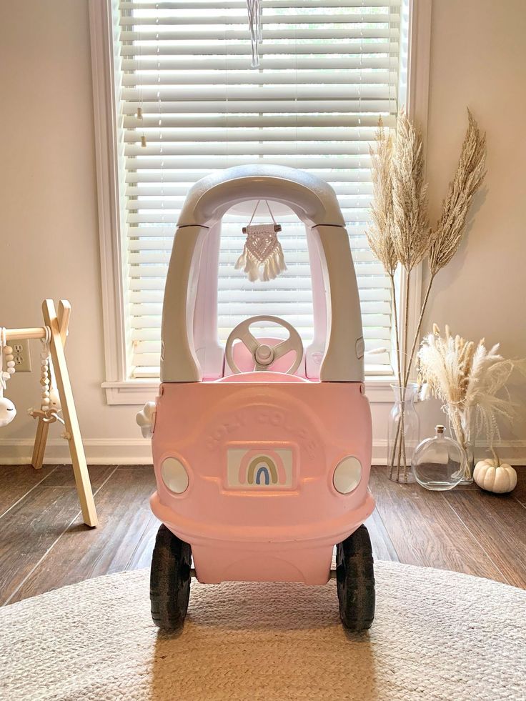 a pink toy car sitting on top of a rug in front of a window with blinds