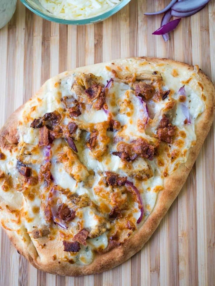 a pizza sitting on top of a wooden cutting board next to a bowl of onions