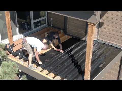 two men working on the roof of a house with black tarp and wood shinning