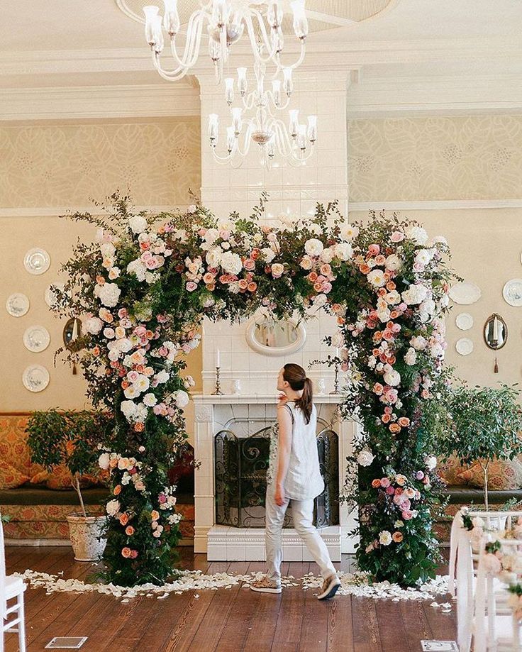 a woman standing in front of a white fireplace surrounded by pink and white flowers on the mantle