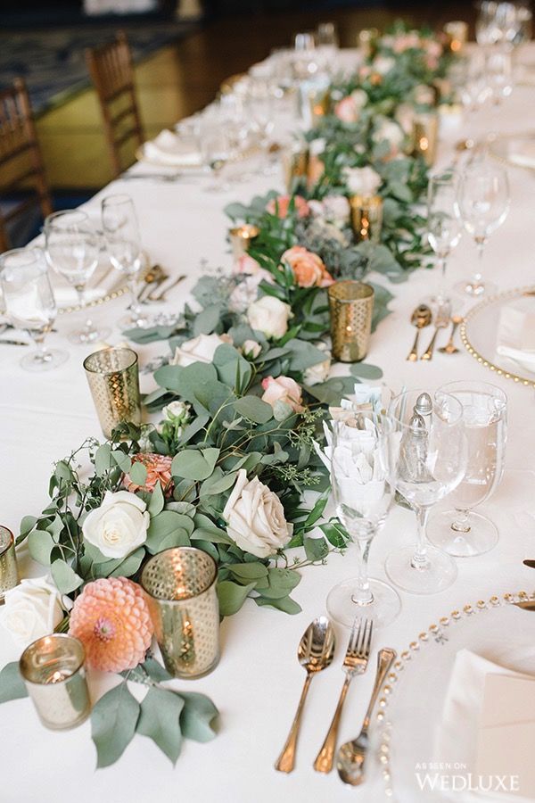 a long table is set with white and pink flowers, greenery and gold candlesticks