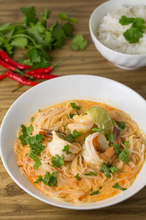 a bowl of shrimp and noodle soup on a wooden table with red chili peppers