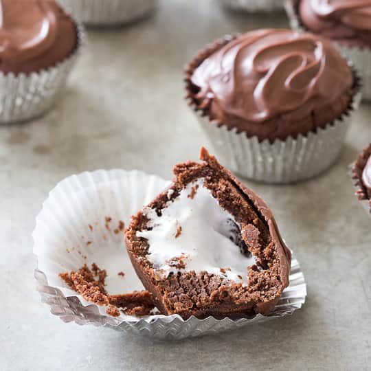 chocolate cupcakes with white frosting and one cut in half on a table