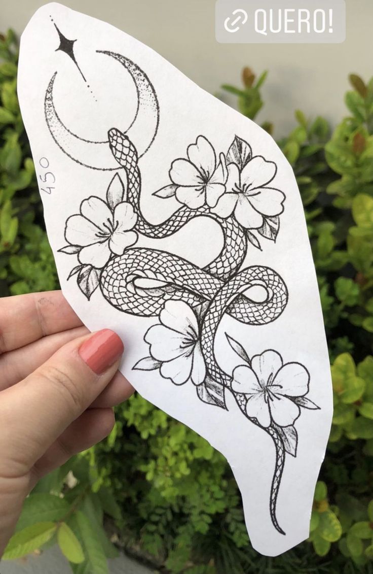 a hand holding up a sticker with flowers and a snake on it's side