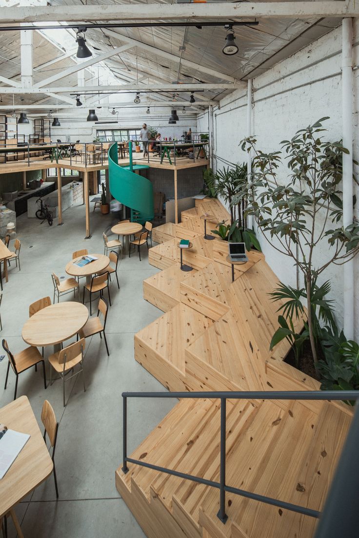 an indoor restaurant with wooden tables and chairs, plants on the side wall and potted trees in the middle