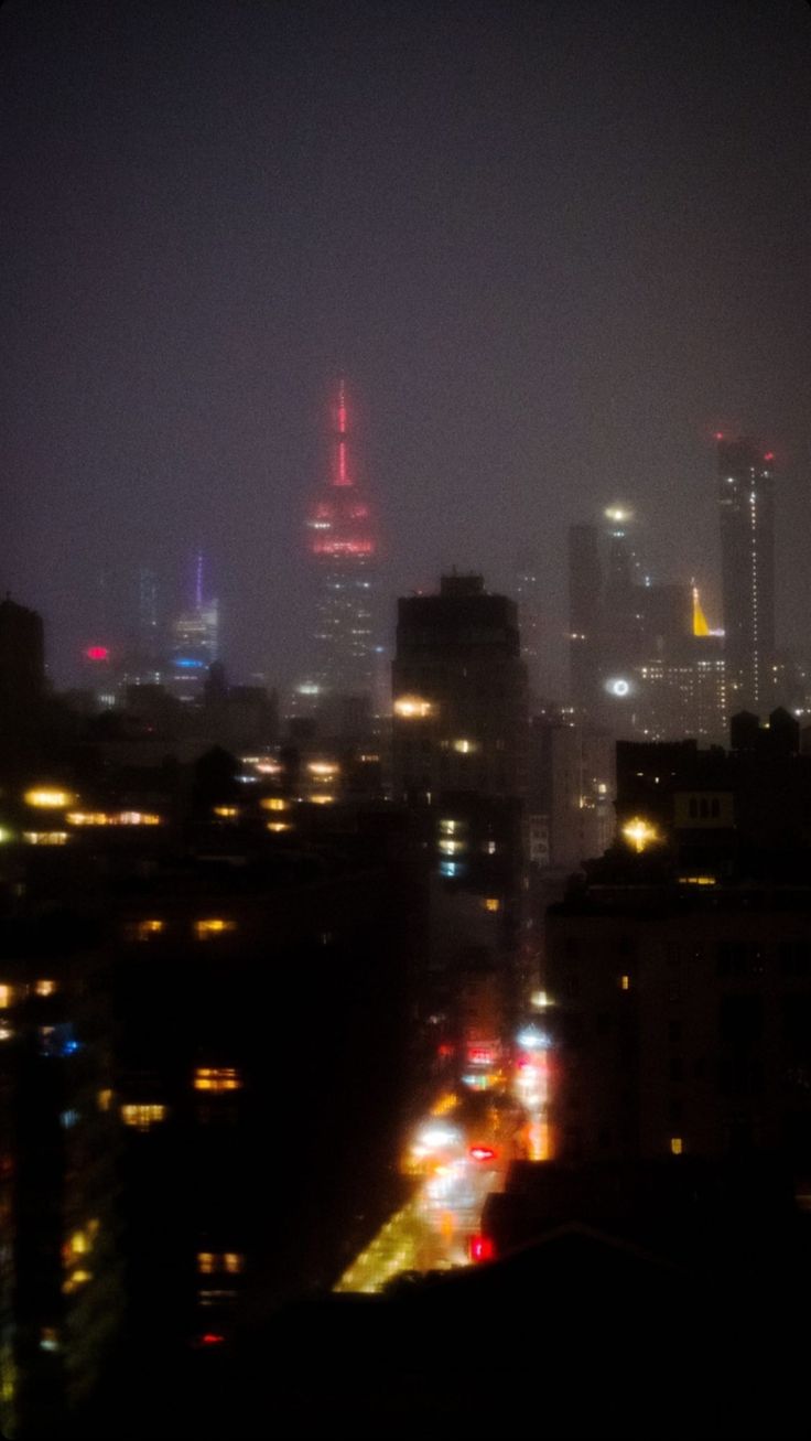 the city skyline is lit up at night, with bright lights in the sky and buildings on either side