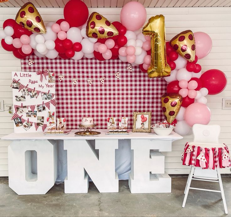 a table topped with balloons and pizza slices next to a sign that says one on it