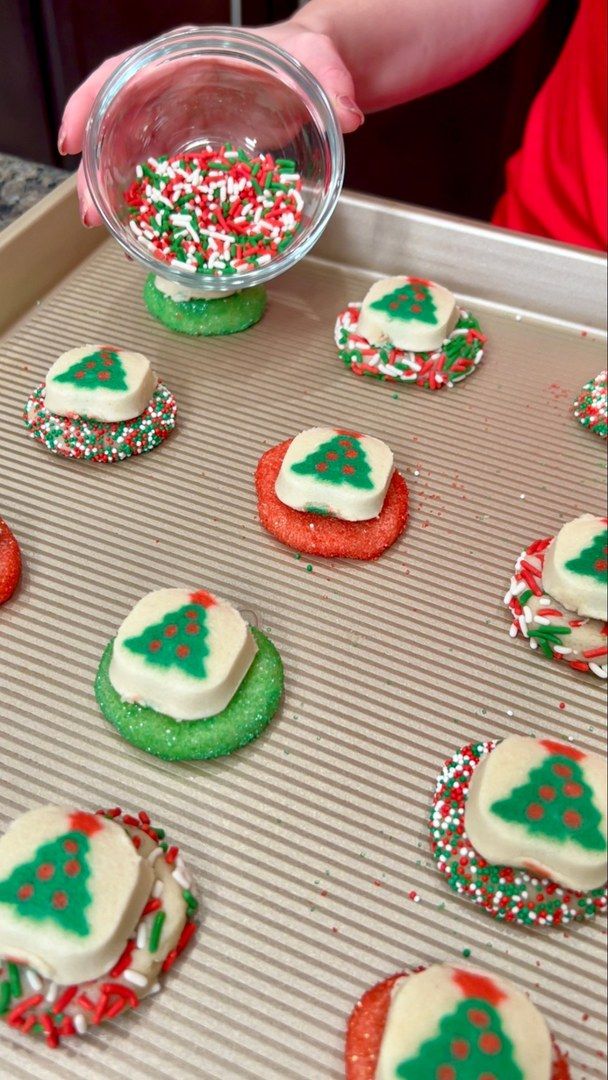 someone is decorating christmas cookies with icing and sprinkles on a baking sheet