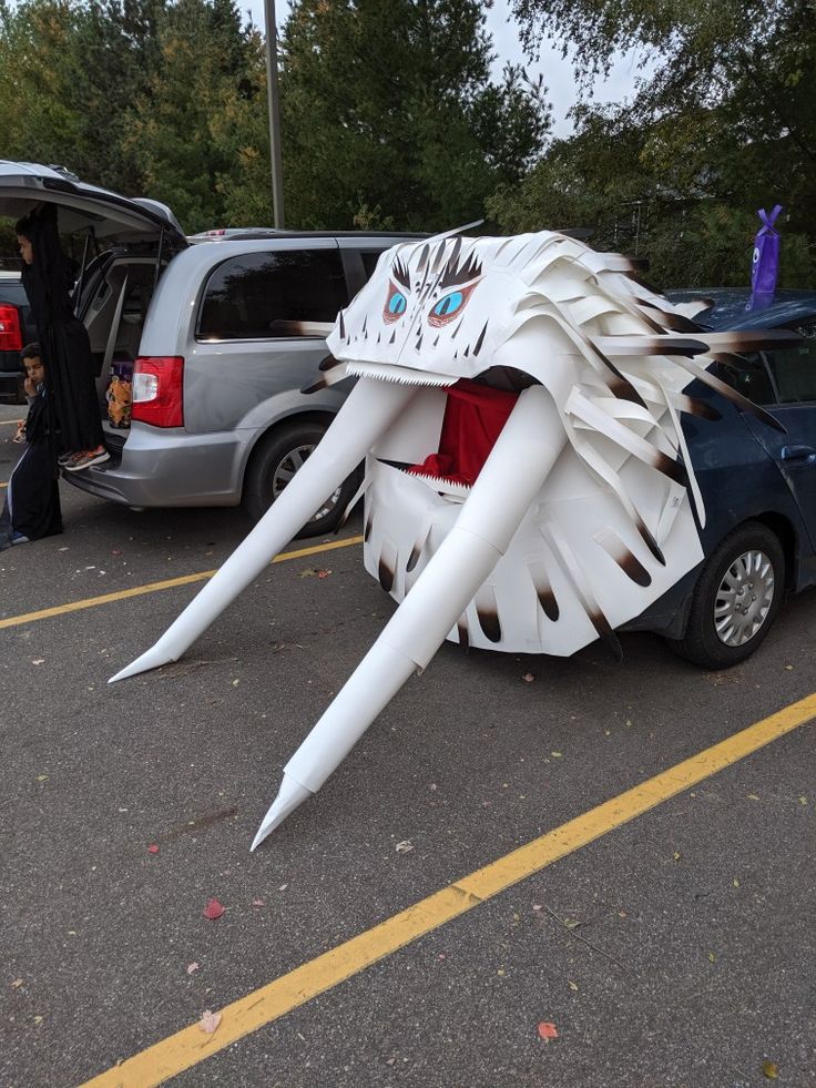 a large white dragon sculpture sitting in the middle of a parking lot next to parked cars