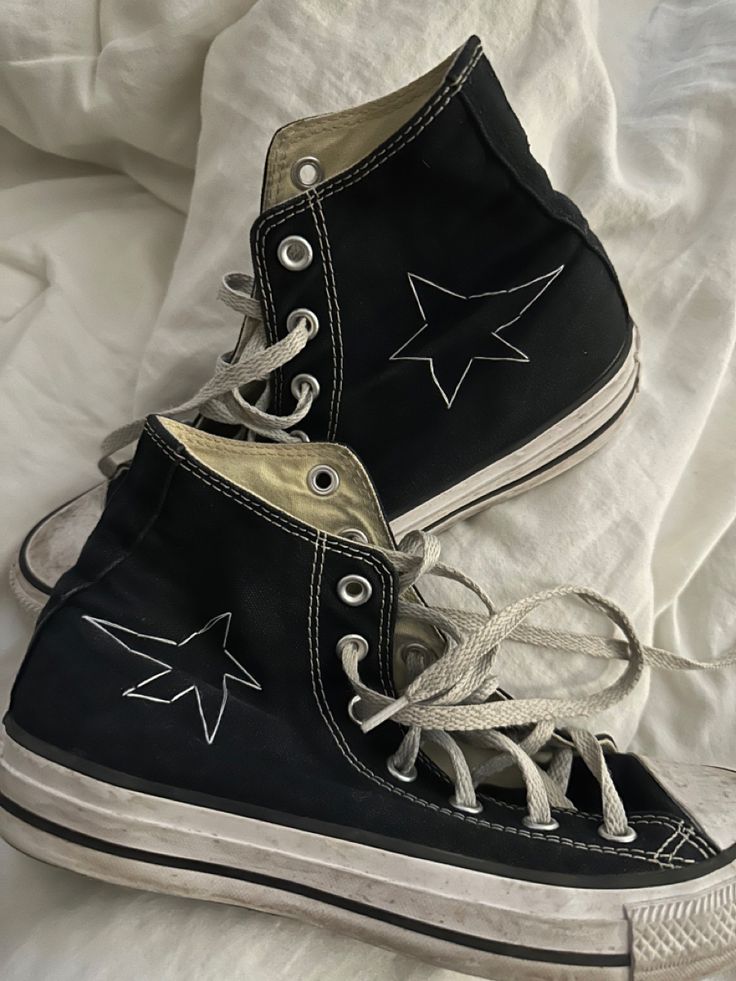 two pairs of black and white shoes with stars painted on the soles are laying on a bed