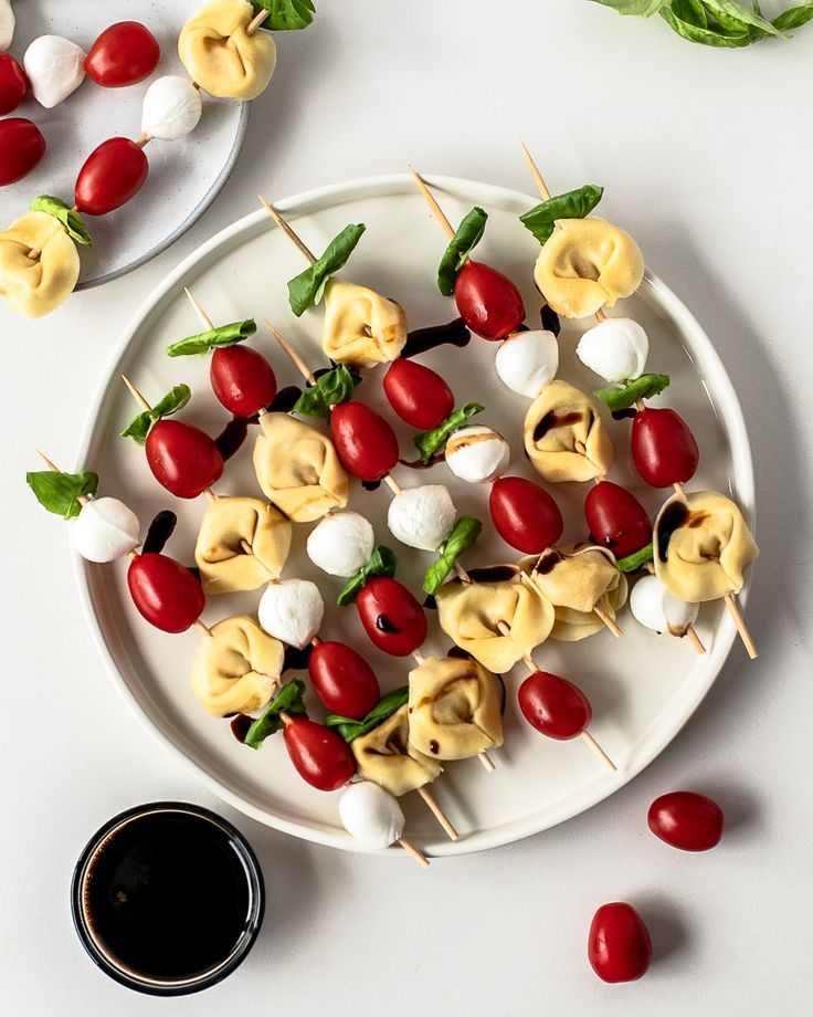 a white plate topped with veggies and pasta on skewers next to sauce